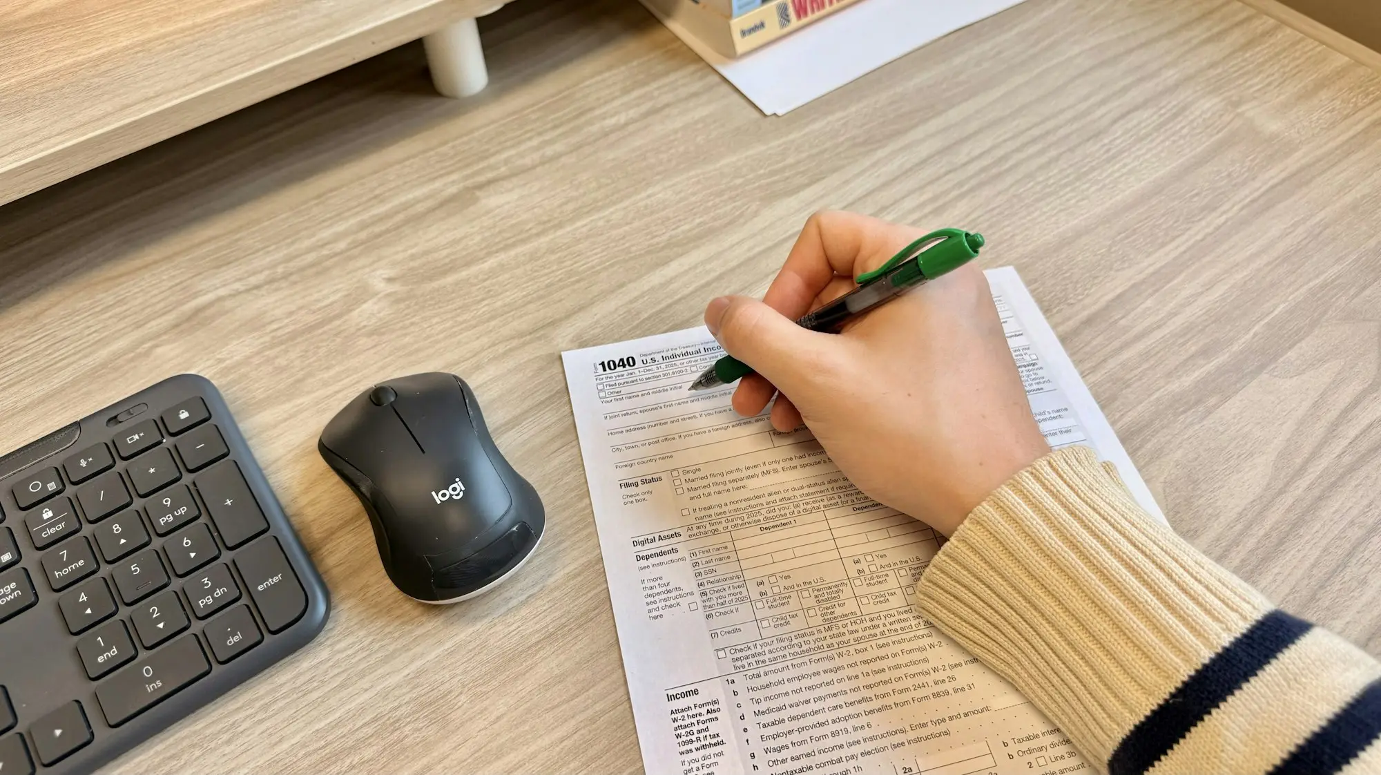 Hand writing on a business document beside a keyboard and mouse while preparing loan paperwork