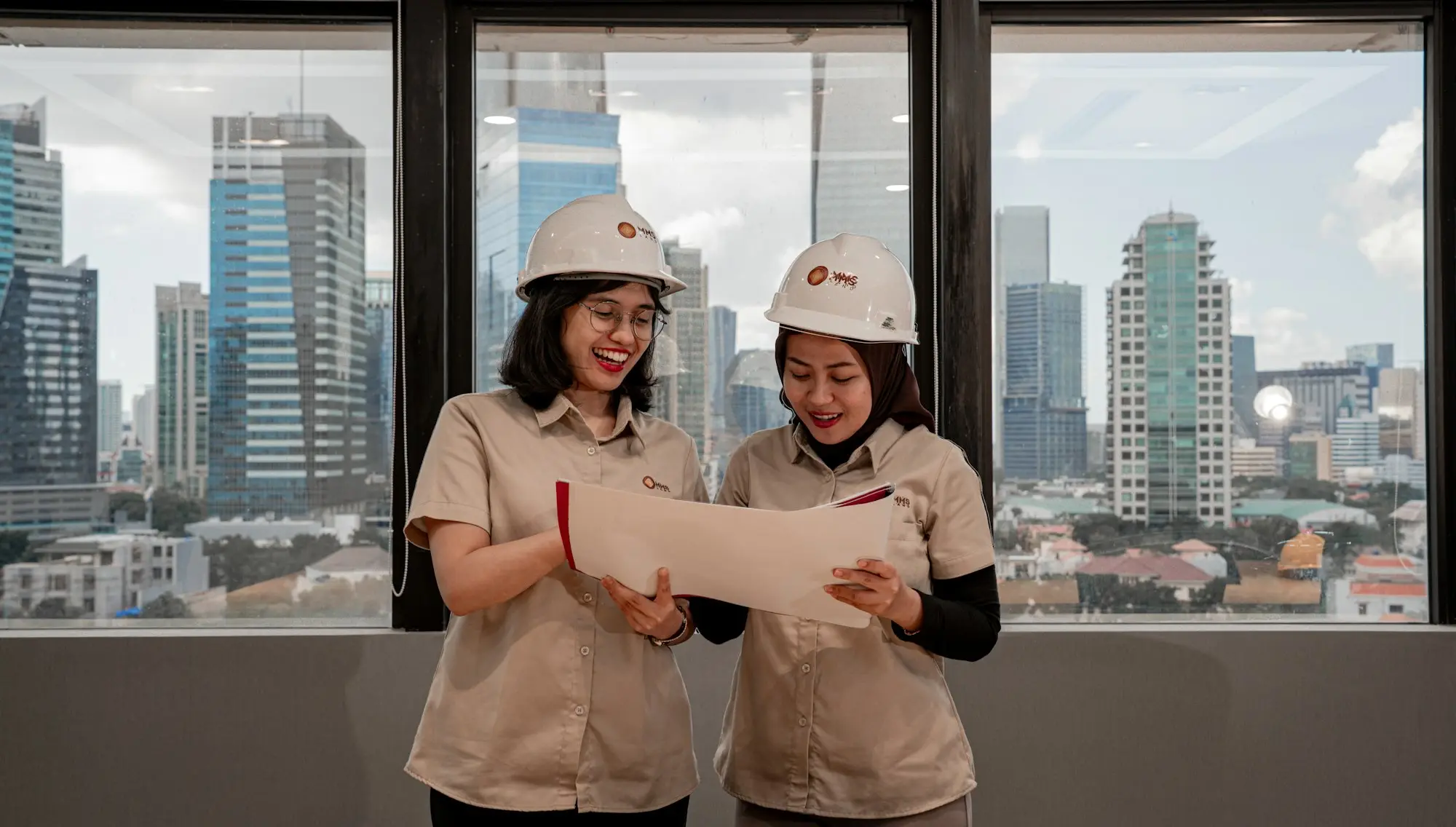 Two women in hard hats reviewing building blueprints indoors before a construction job